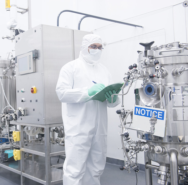Man in lab clothes in front of a fermenter.